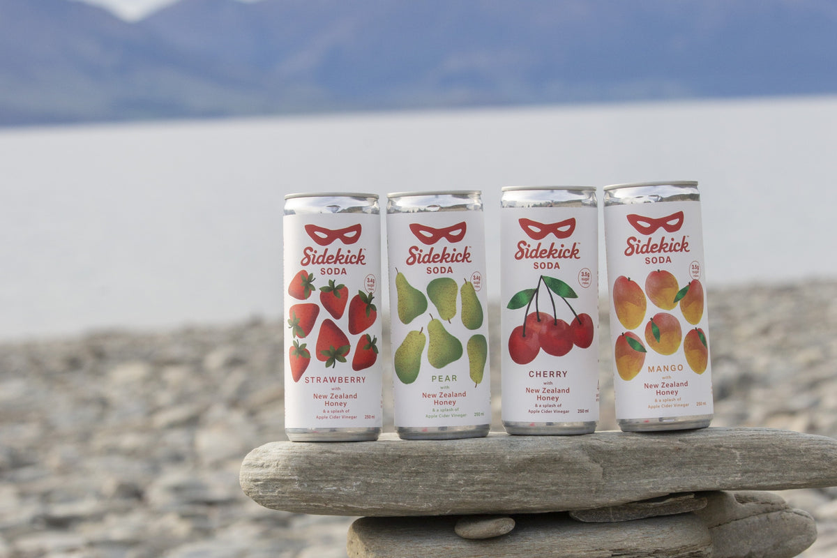 Sidekick Soda cans on lake stones — Strawberry, Pear, Cherry, and Mango